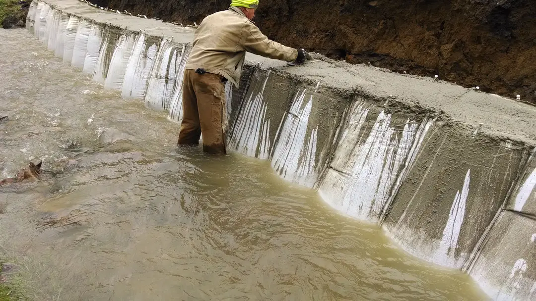 A man in brown pants and yellow hat standing next to water.