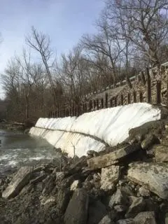 A large amount of snow is on the rocks near the water.