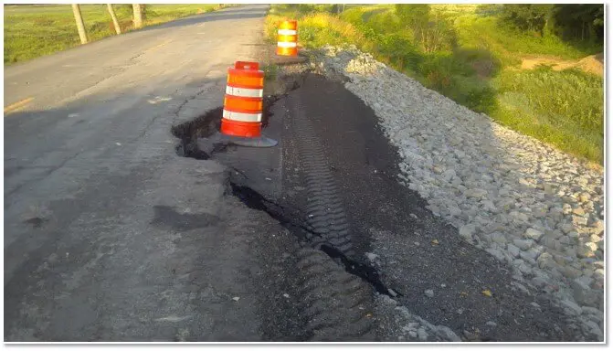 A road with a broken asphalt and a cone.